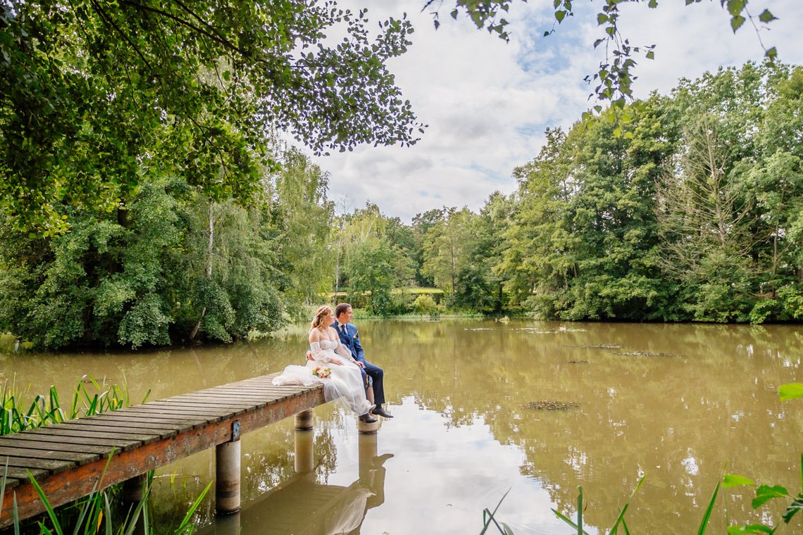 Brautpaar sitzt auf Steg am Teich in Adams Gasthof